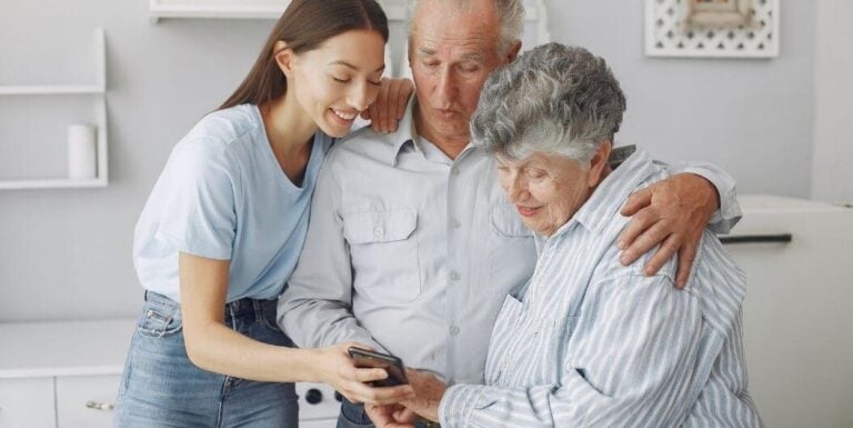 Young Woman Showing Phone to Elderly Couple and Smiling at Independent Living Facility
