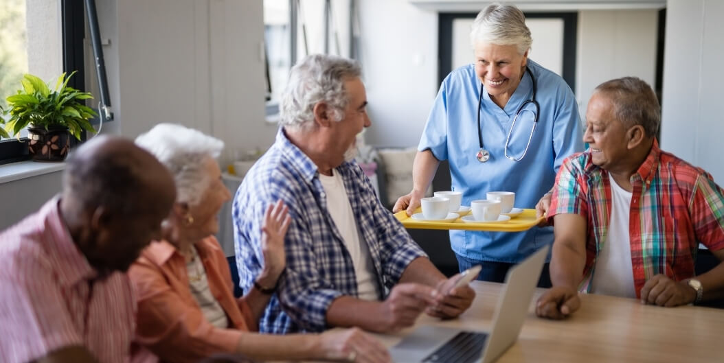 Elderly Group Chatting With Nursing Staff Over Coffee in Independent Living