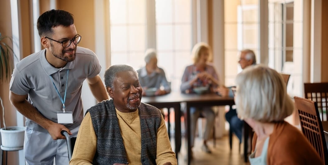 Male Nurse Assisting Senior Man in Dining Area at Independent Living Facility