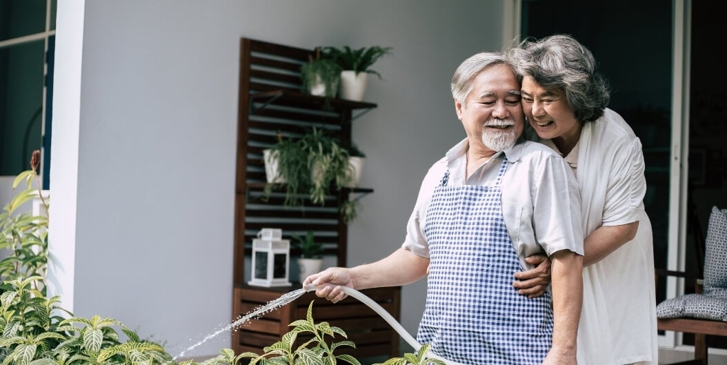Elderly Couple Watering Plants Together Outside at an Independent Living Facility