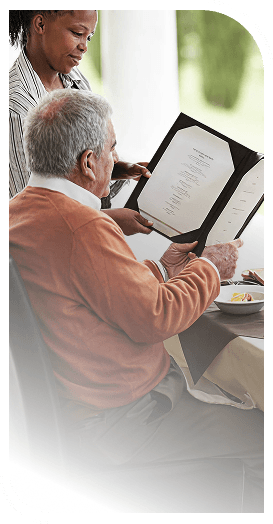 Elderly Man Reading a Dinner Menu With an Attentive Server in Independent Living