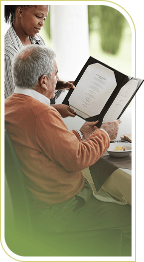 Elderly Man Reading a Dinner Menu With an Attentive Server in Independent Living