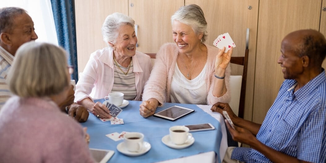 Elderly Friends Laughing Over Card Game and Coffee at Independent Facility